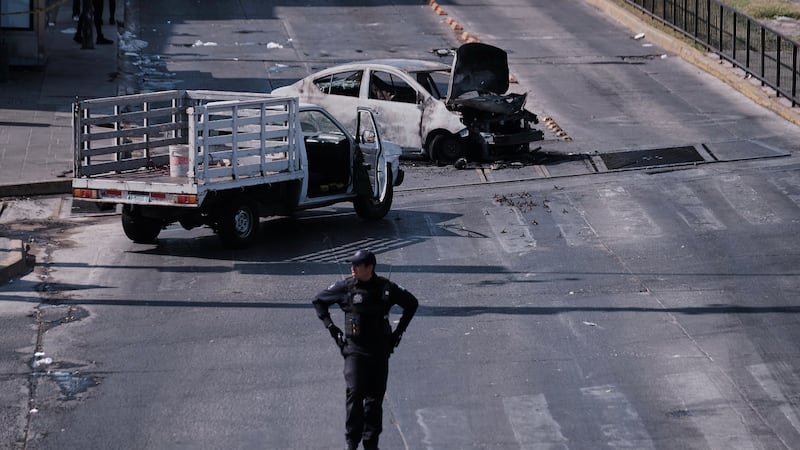 A police officer stands guard by a charred vehicle after it was set on fire, on a road in...